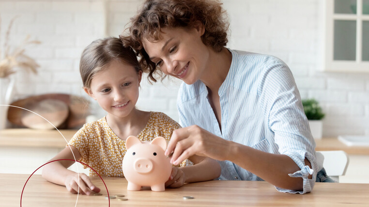 Eine Frau und ein Mädchen sitzen am Küchentisch und befüllen ein rosa Sparschwein mit Geldmünzen.