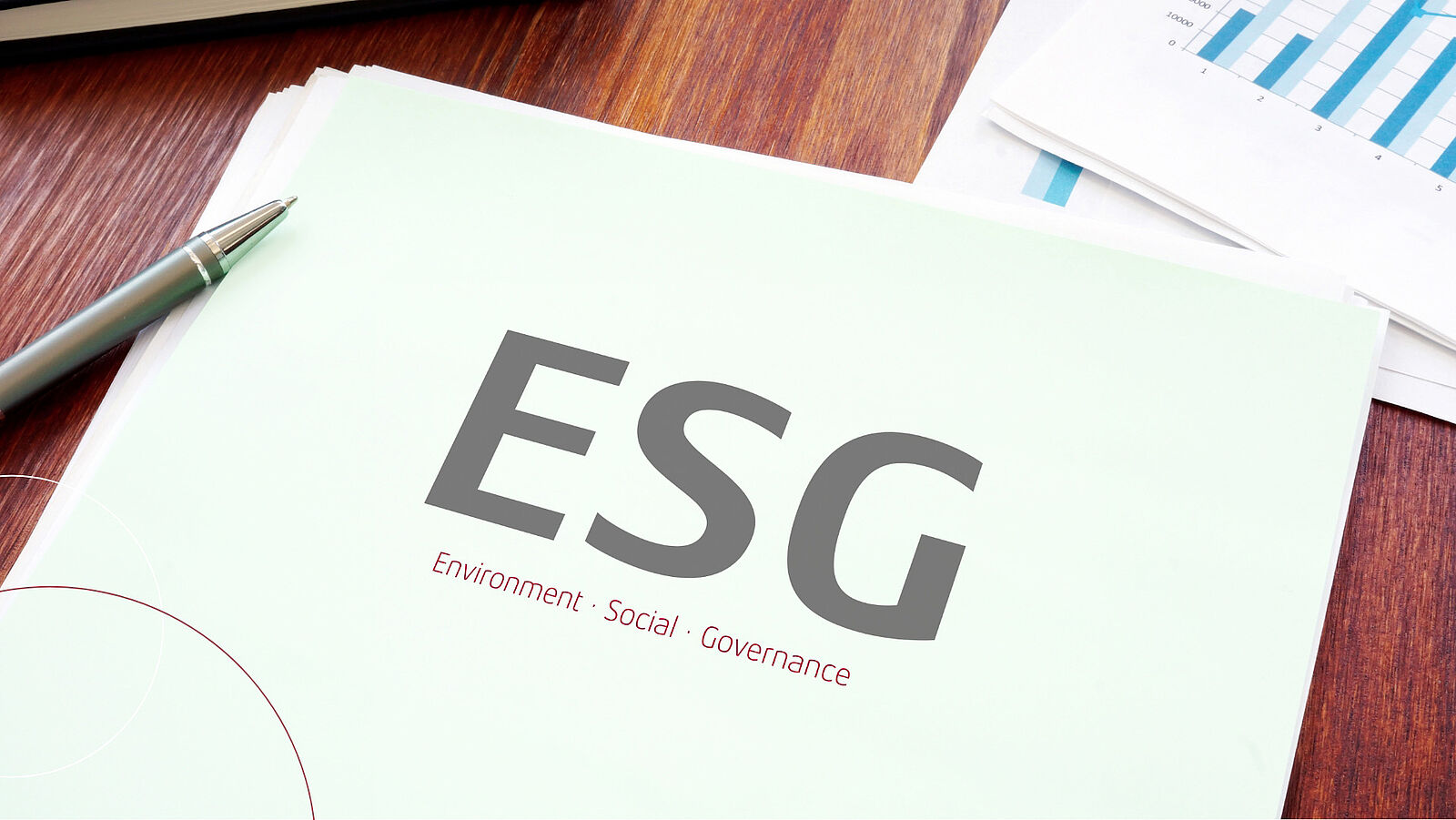 Eine Arbeitsmappe mit der Aufschrift ESG: Environment, Social, Governance liegt auf einem Schreibtisch. Oben rechts in der Ecke sind Ausdrucke von Balkendiagrammen zu sehen.