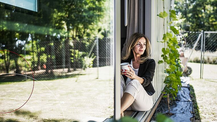 Frau mit einer Kaffeetasse sitzt in einer Glastür